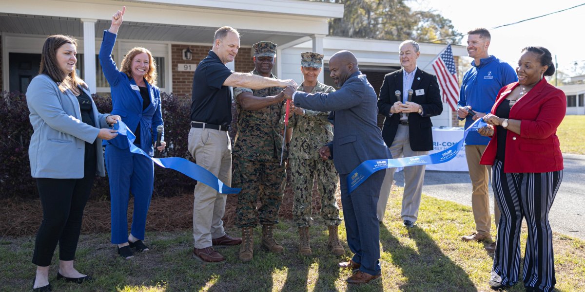 Executives and servicemembers cut a ribbon in front of a newly built house.