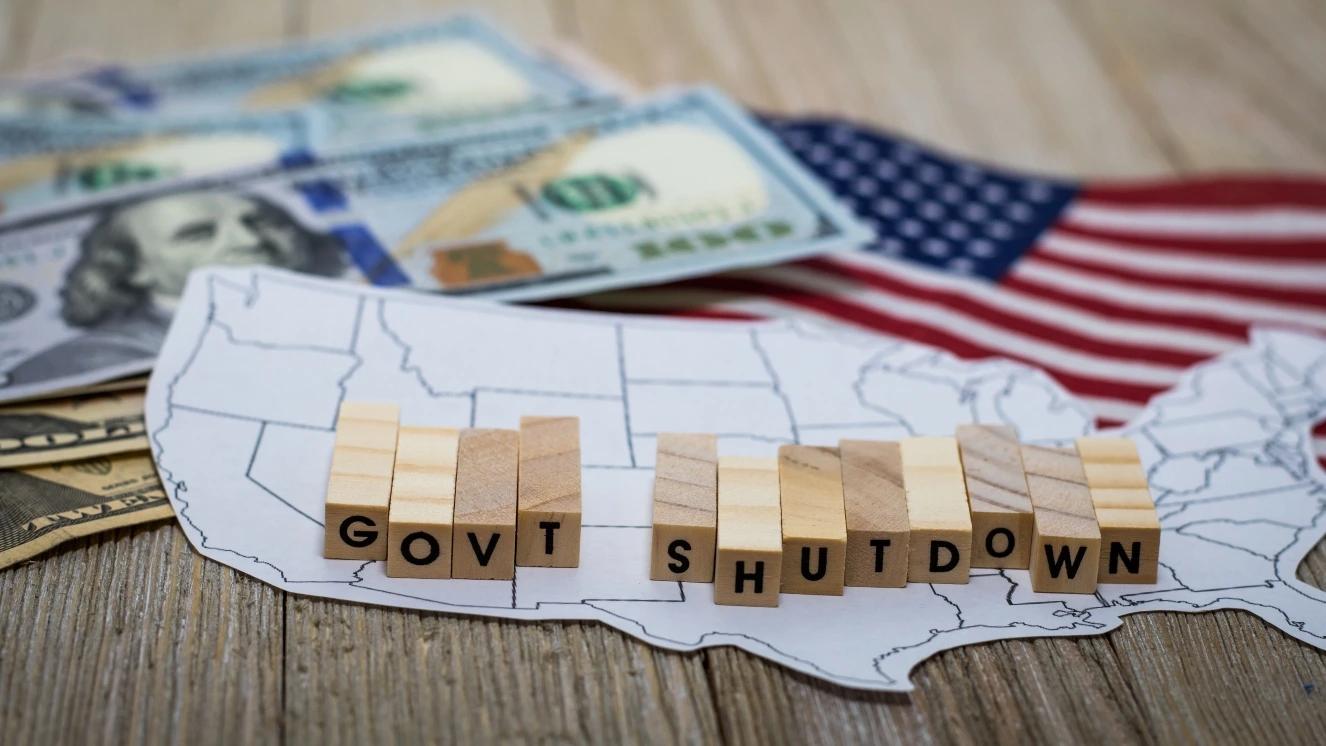 Government Shutdown USA concept with American flag and money bills on white background and wooden board.