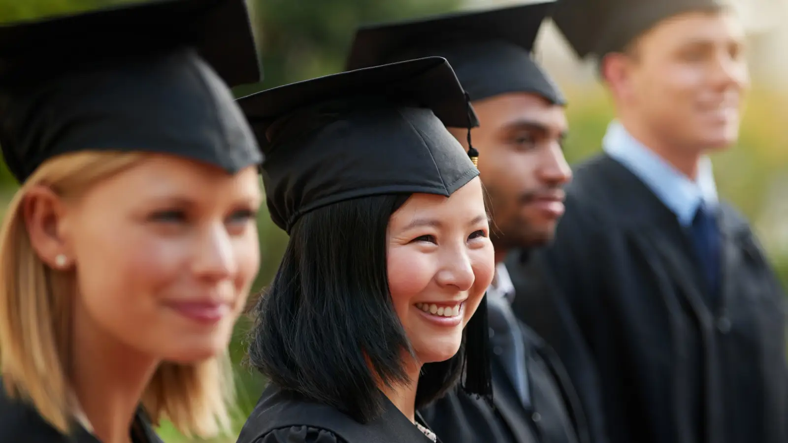 Four College graduates stand in caps and gowns.