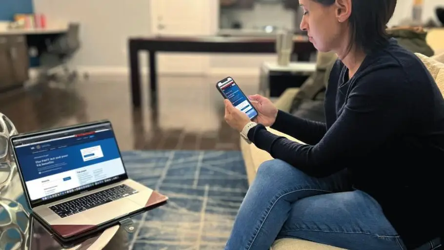 Woman looks at phone and laptop on the VA website.
