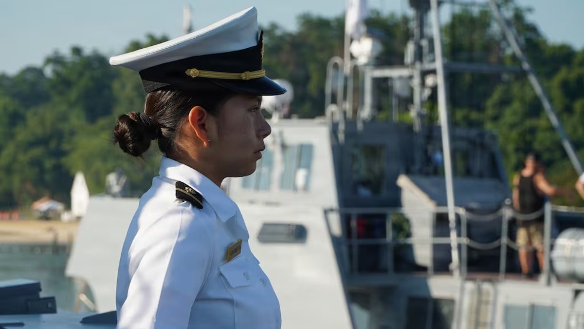 A female midshipman is standing at attention, seen in profile.