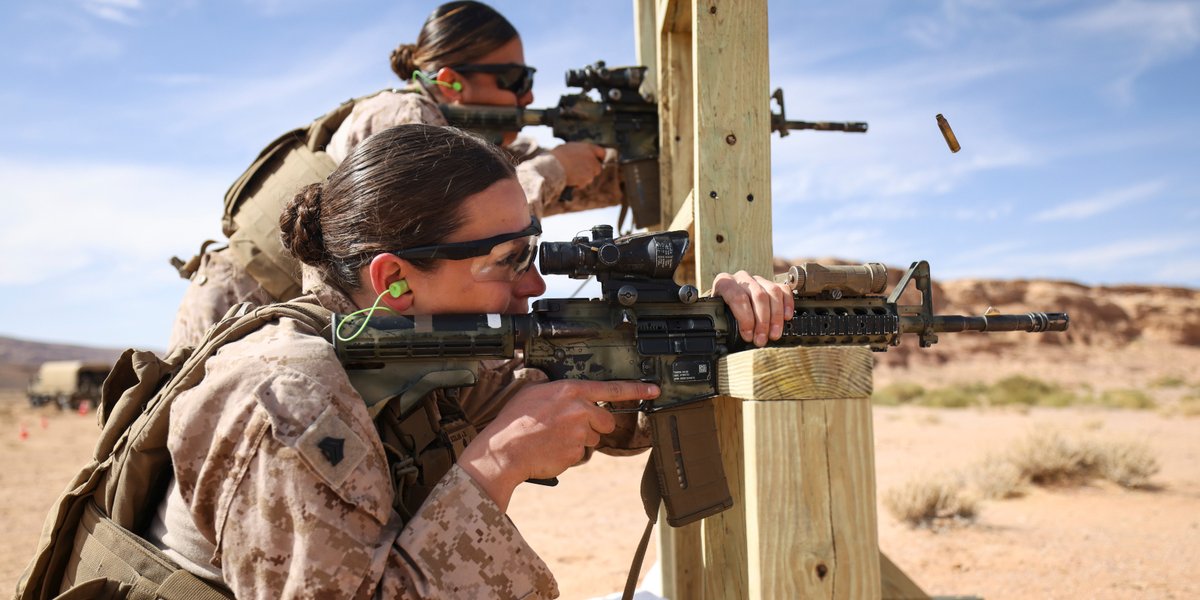Two women in uniform complete combat marksmanship training with rifles on a gun range.