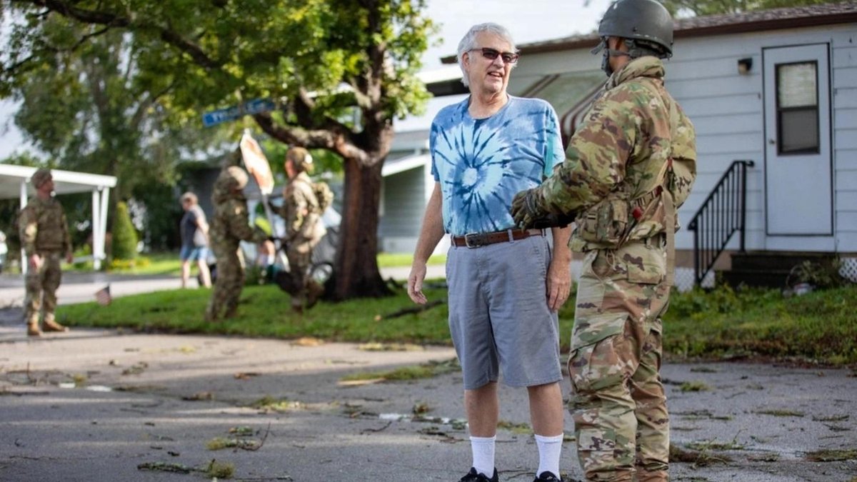 Army National Guard soldier assisting a civilian on a debris-strewn street.