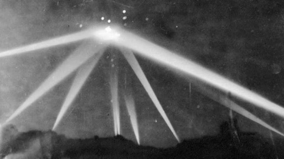 Vintage photo of searchlights pointing at an explosion in the sky.