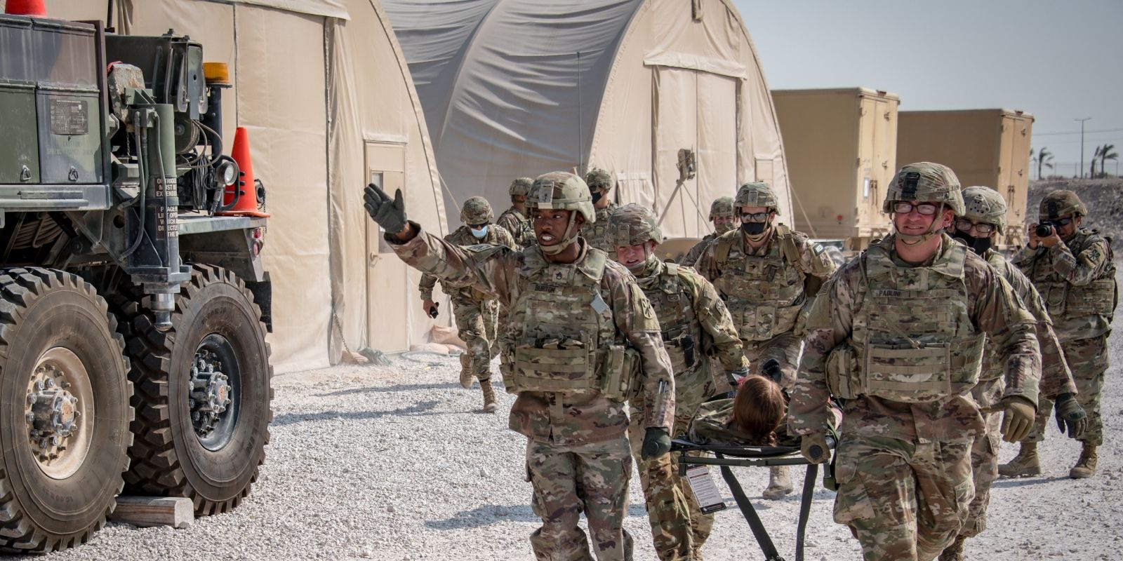 A dozen soldiers carry another serviceman on a gurney in a training exercise in Doha, Qatar.