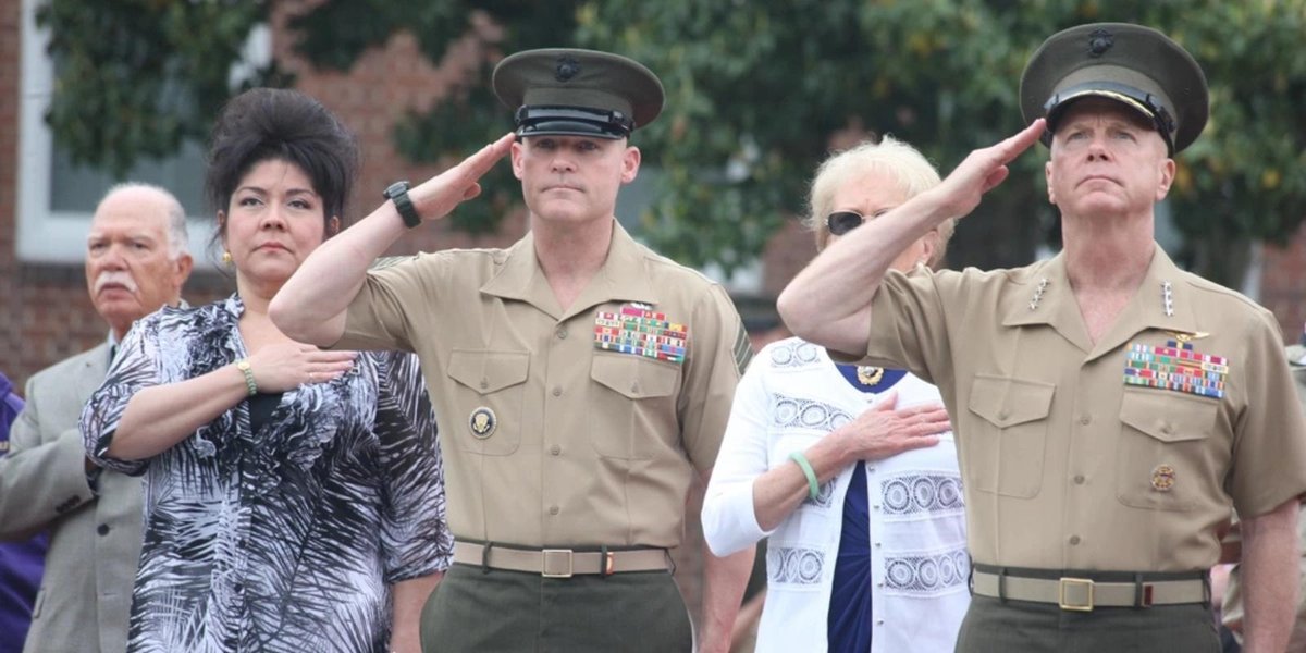 Marine Corps officers saluting during a ceremony alongside civilians.