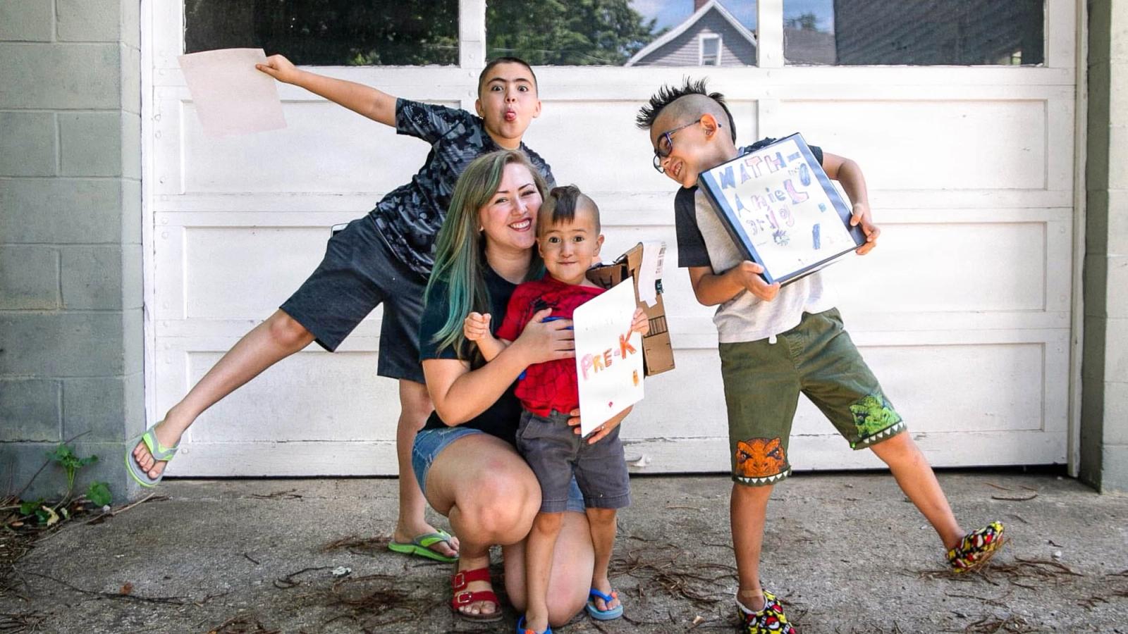 A mom has fun posing in the driveway with her three boys.