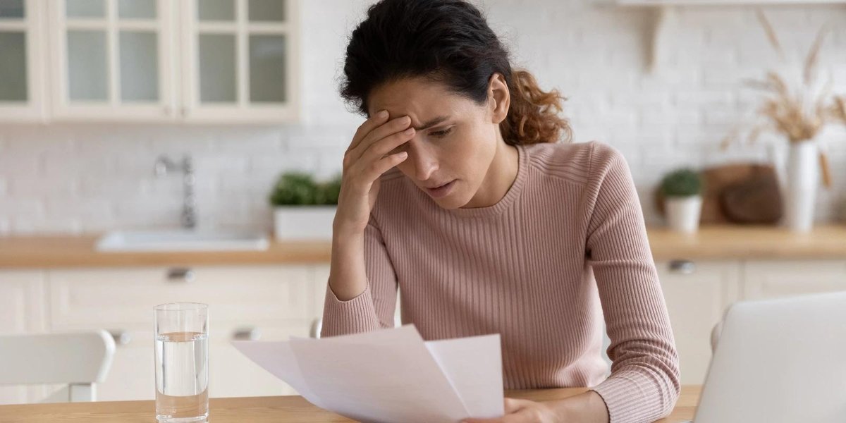 Woman reviewing documents at kitchen table, looking concerned