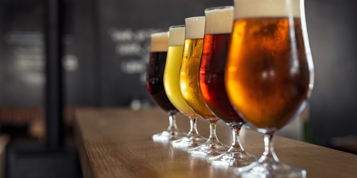 Five glasses of different beers on a bar counter.