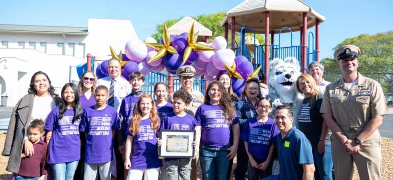 Capt. Brian Bungay, commanding officer, Naval Base San Diego (NBSD), middle, Command Master Chief Kristopher Freyberg, right, and Hedenkamp Elementary students and staff pose for photo during the Purple Star ceremony held at Hedenkamp Elementary School, Apr. 10, 2026. 