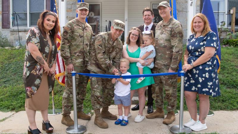 Col. Matthew Poisson, center, individual mobilization augmentee to the 66th Air Base Group commander, and Cooper Fontenot, prepare to cut a ribbon to officially open a new Family Child Care program managed by Sydney Fontenot, center right, in family housing at Hanscom Air Force Base, Mass., Aug. 5.
