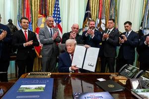 Trump signs executive order surrounded by supporters.
