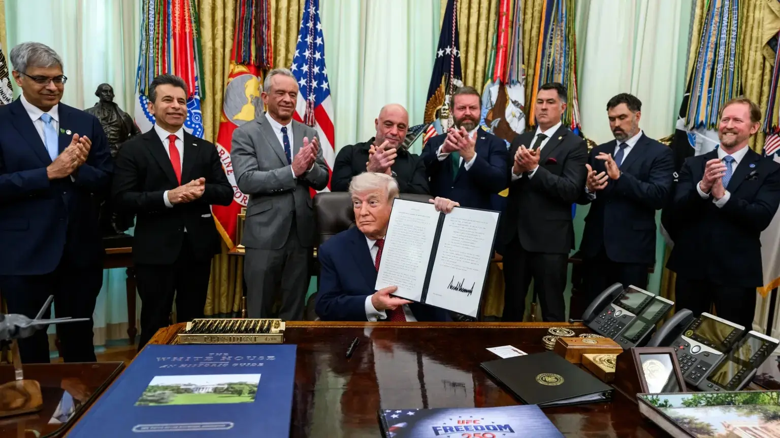 Trump signs executive order surrounded by supporters.