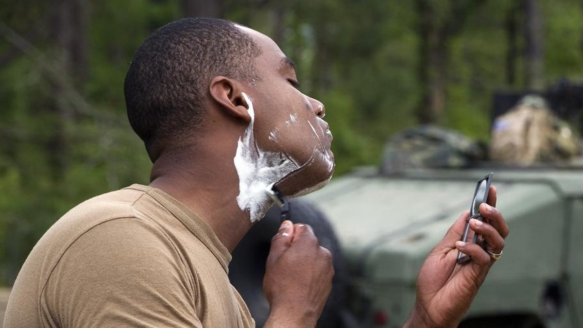 A black Marine uses a mirror to shave outdoors.