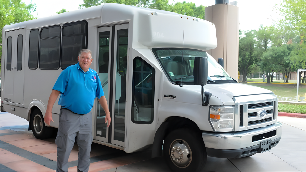 A man stands in front of a motor vehicle.