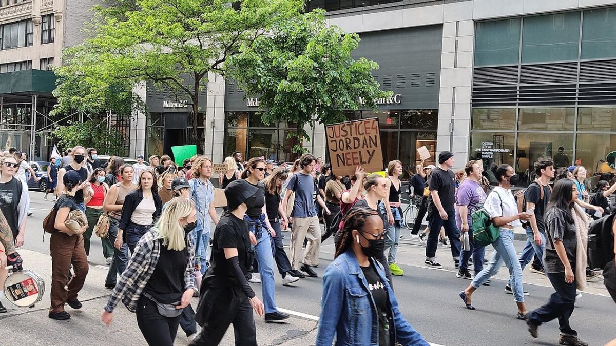 Protesters marching with "Justice for Jordan Neely" sign on city street.