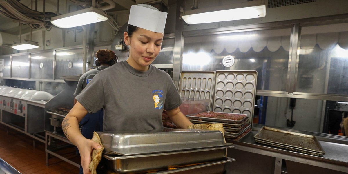 U.S. Navy Culinary Specialist Seaman Apprentice Ne’Coe Mitchell carries hot pans to the oven in the aft galley of Nimitz-class aircraft carrier USS Abraham Lincoln (CVN 72) on Nov. 23, 2025. 