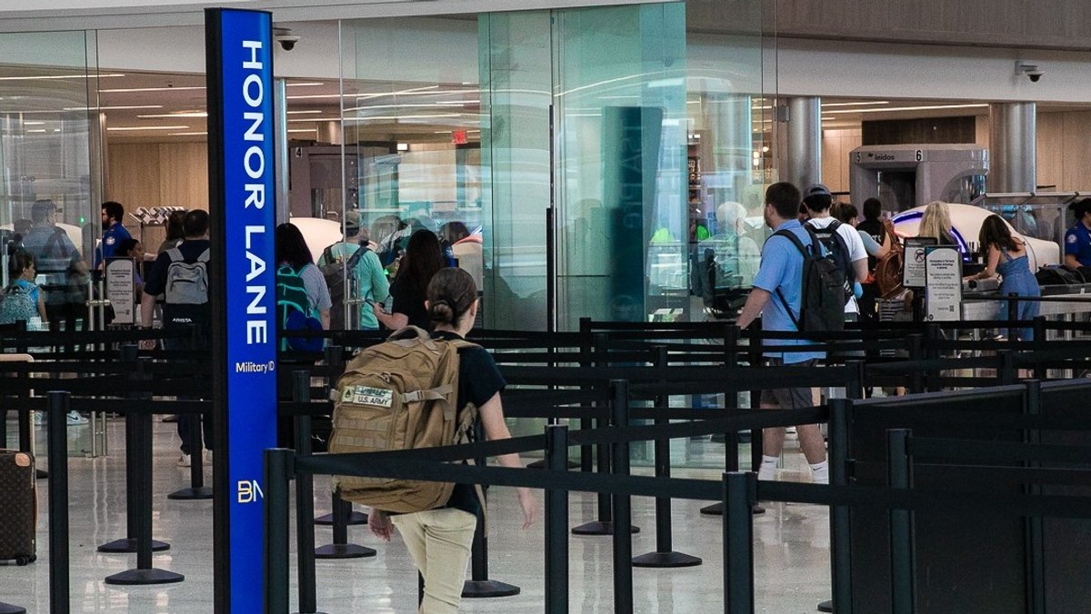 A young woman with a backpack walks into a zigzag web of the Honor Lane at the airport.