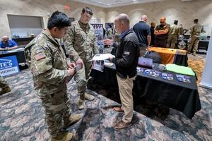 Two soldiers discuss benefit packages with a broker at a fair.
