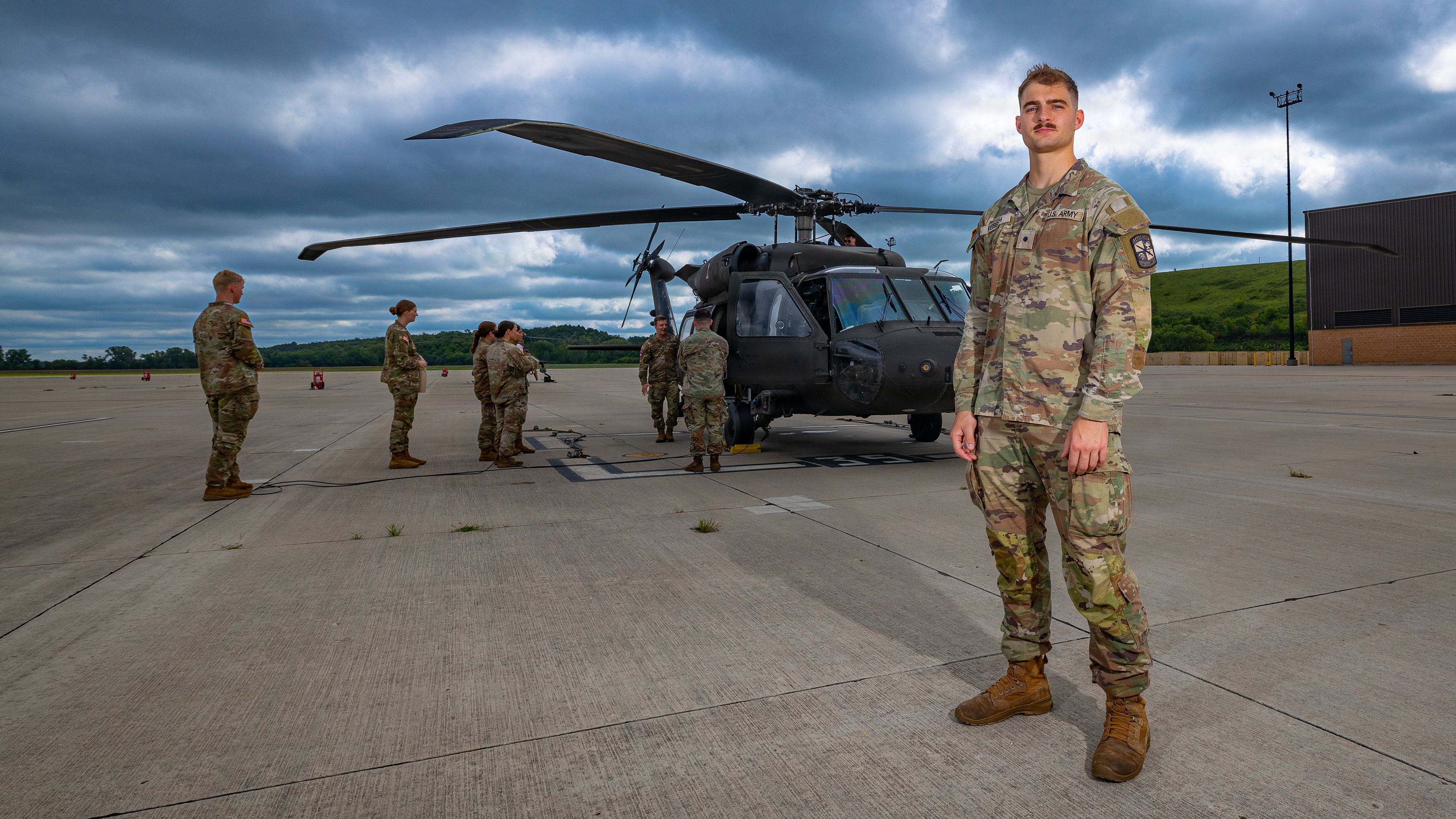 A soldier stands apart from other service people on a tarmac in front of a helicopter.
