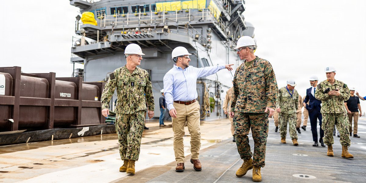 Three men walk on a ship, taking a tour.