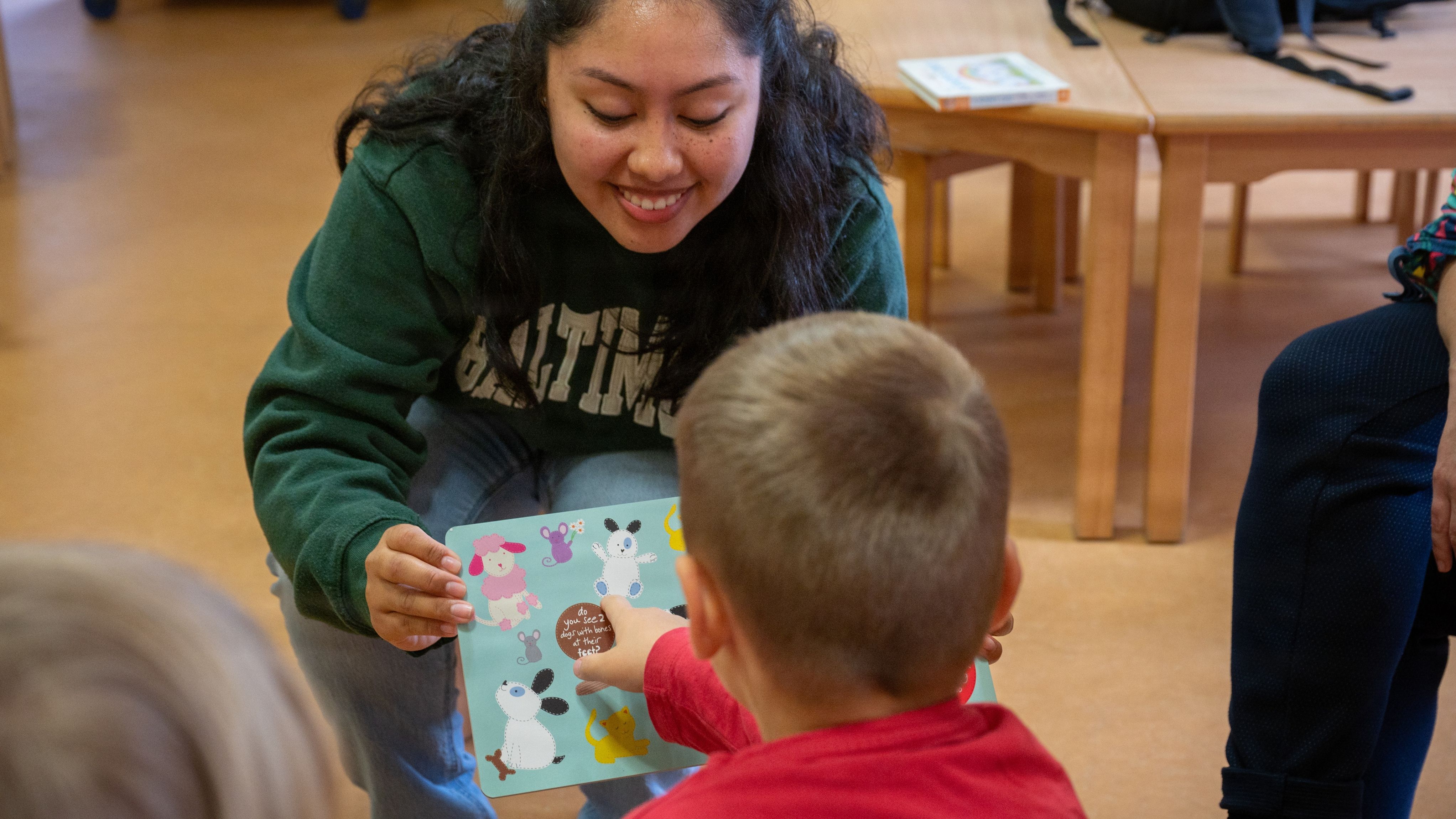 A woman shows a book to a toddler in a childcare center.