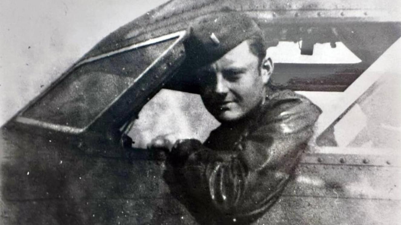 WWII pilot in leather jacket leaning out of aircraft cockpit window