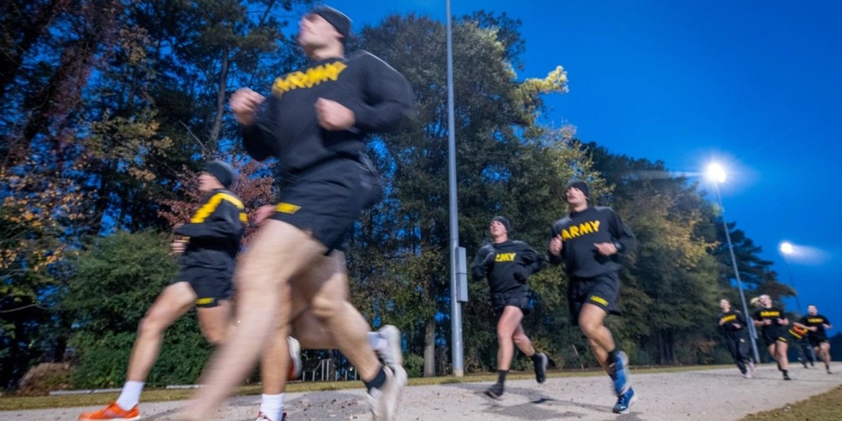 Army soldiers jogging on a wooded trail during early morning training