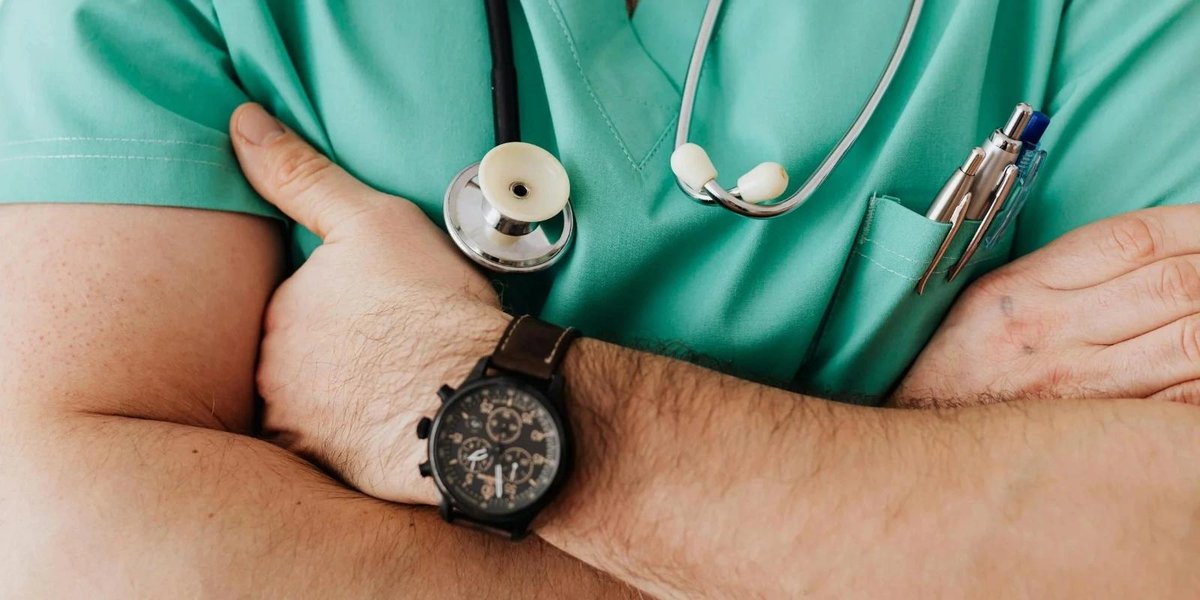 Military healthcare professional in scrubs with stethoscope and watch, arms crossed.