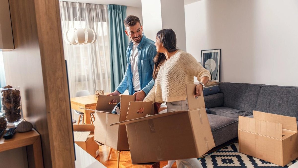 Couple unpacking boxes in new home living room, discussing VA home loan benefits.