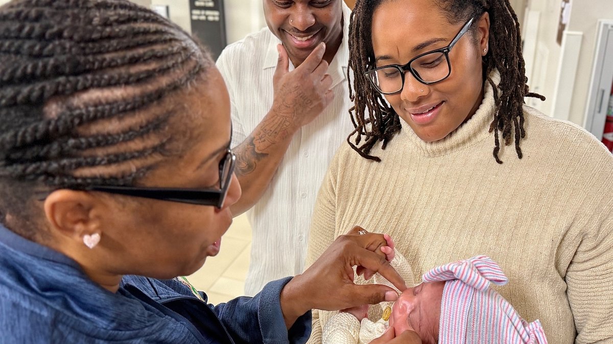 A new mother and father hold a baby while receiving care education from a military nurse.