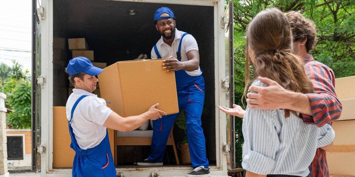 Movers unloading boxes from a truck while a couple observes, related to PCS moving companies.