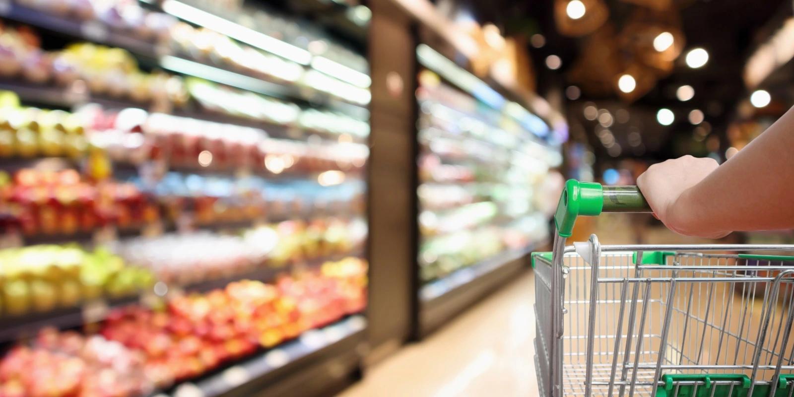 Person pushing shopping cart in grocery store aisle with shelves of colorful products