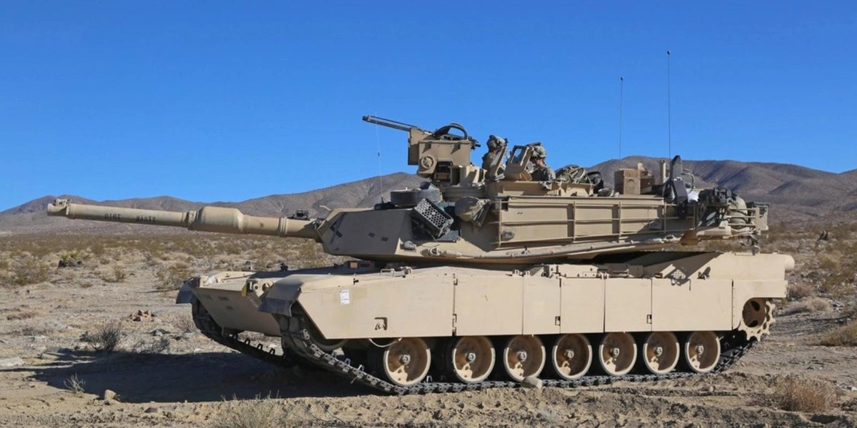 M1 Abrams tank in desert terrain with crew visible on turret