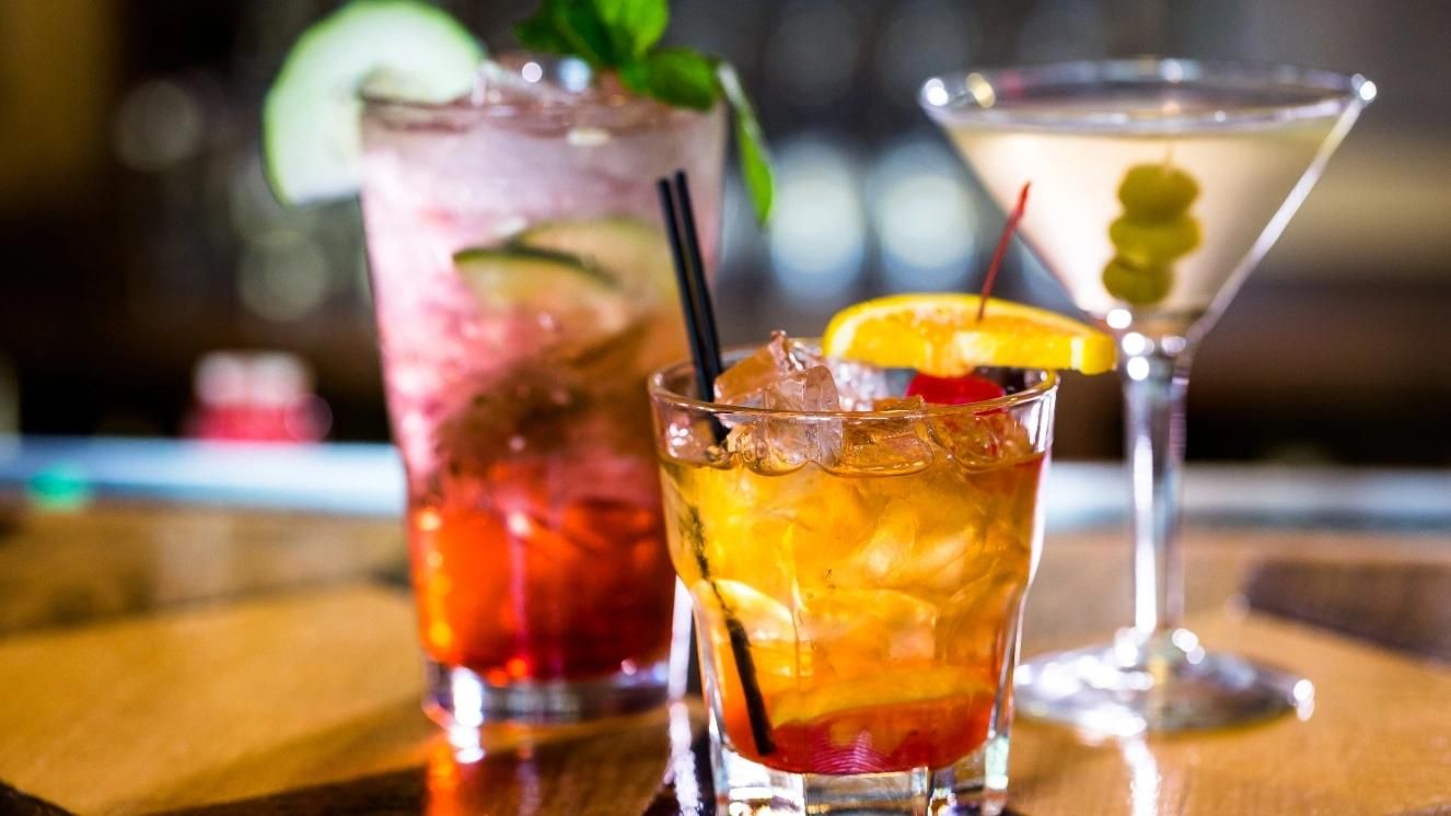 Cocktails on bar top with garnish, featuring a martini with olives and two mixed drinks with fruit.