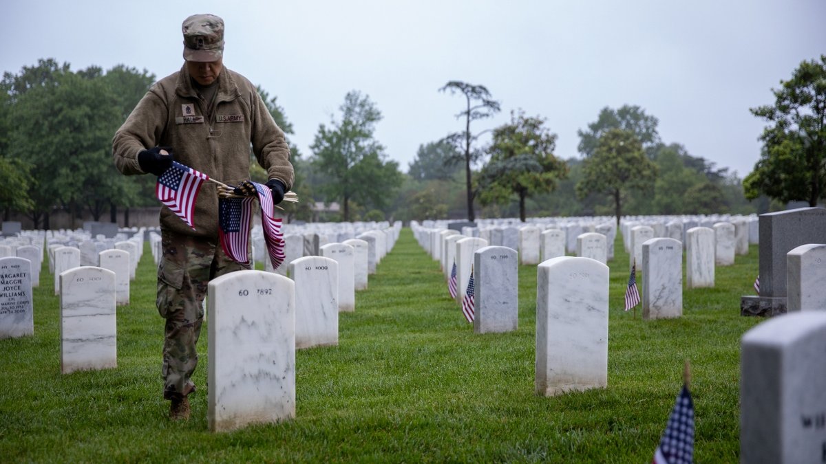 An Army sergeant places flags at headstones in Arlington Cemetery.
