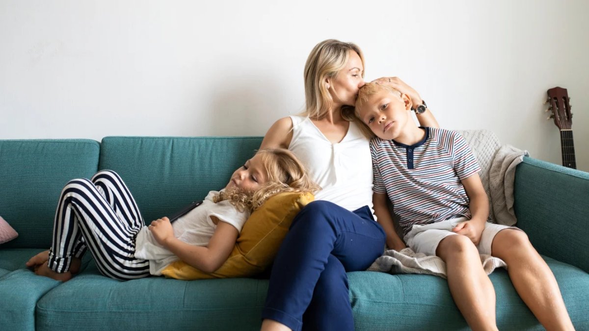 Military spouse comforting children on living room sofa during deployment