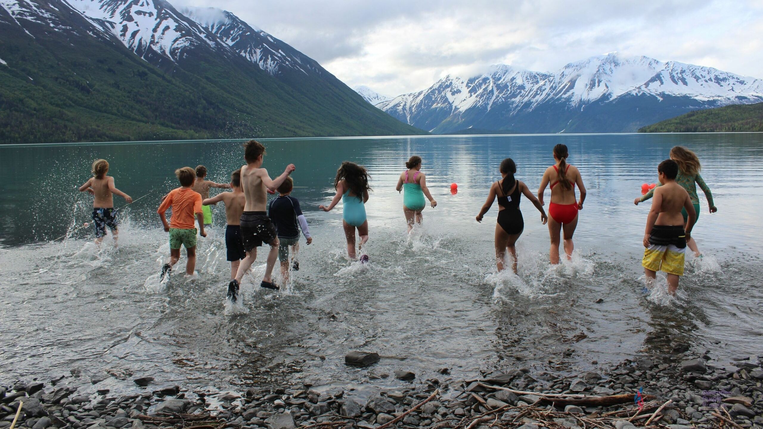 A big group of kids run and jump in a lake.