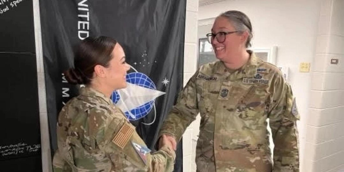 Space Force Guardians in uniform shaking hands indoors near Space Force flag.