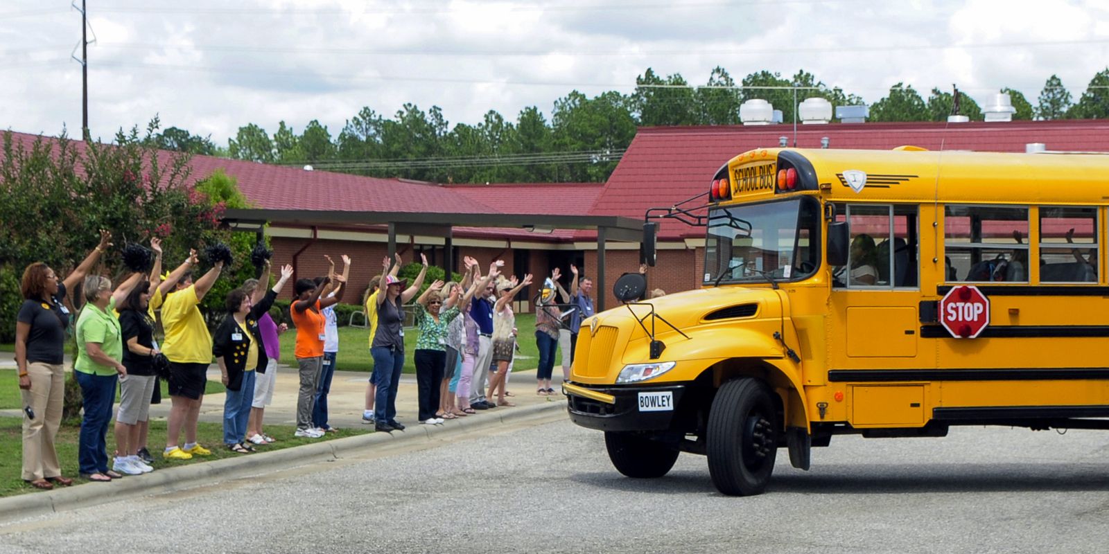 Kids coming to school on a bus with teachers waiving.