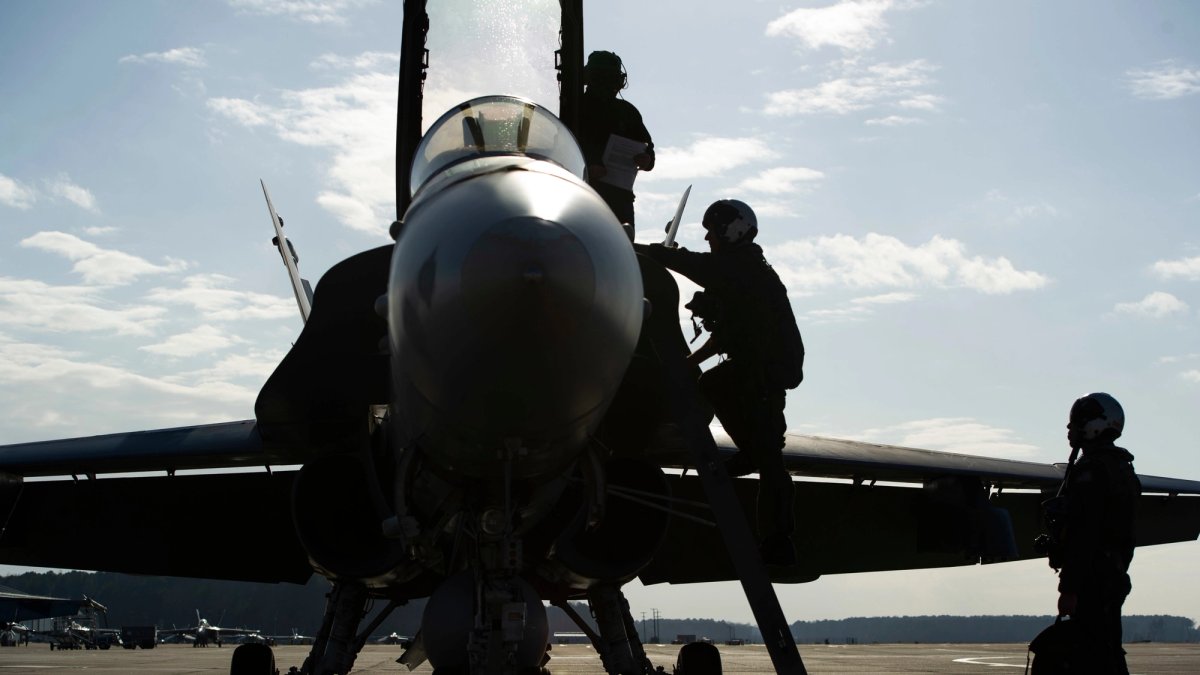 Three aviators stand outside of a fighter jet.