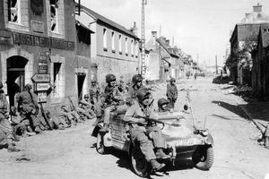 A vintage black and white photo of US soldiers driving through a bombed-out French town.
