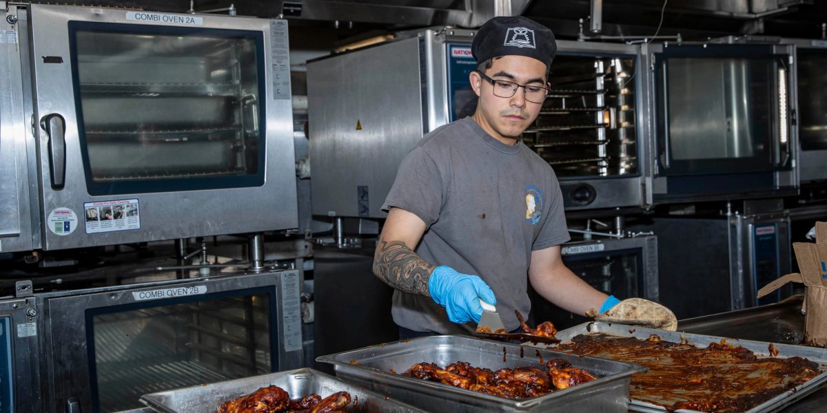 A food worker arranges chicken in a serving tray.
