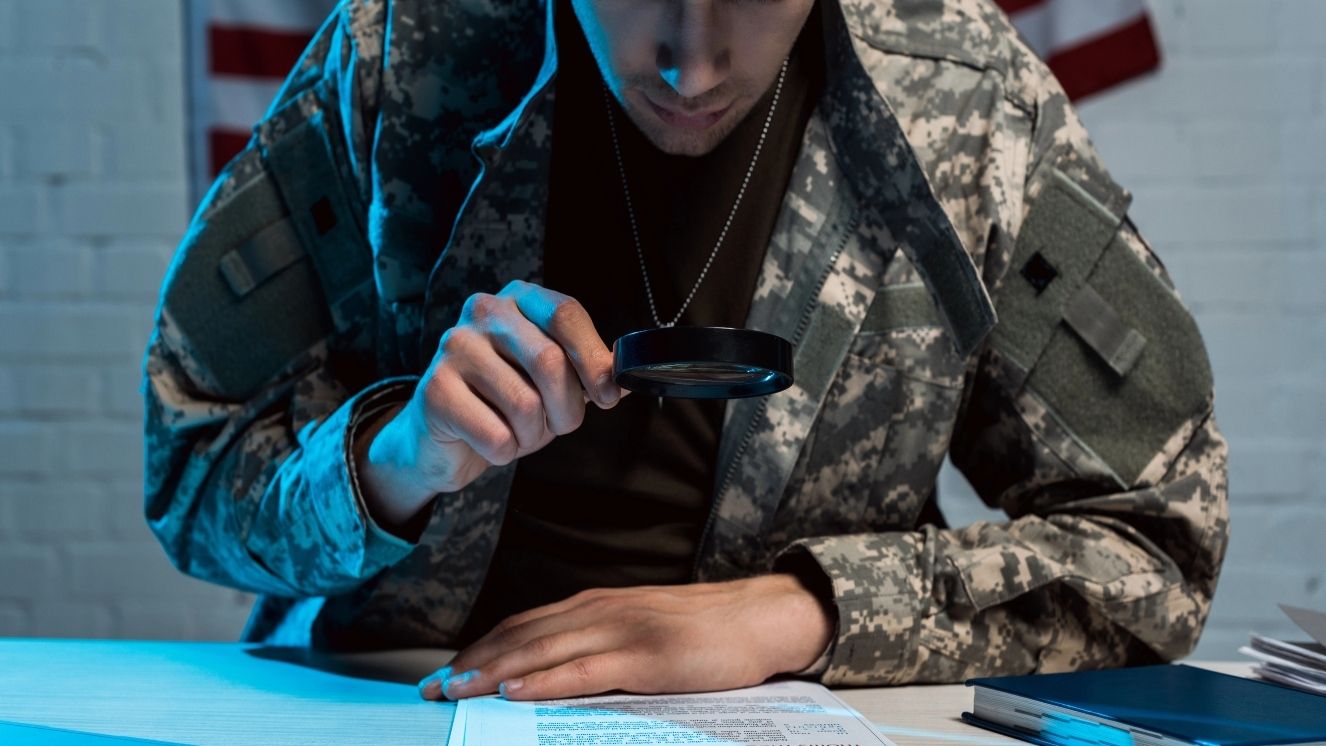 Soldier reads papers with a magnifying glass.