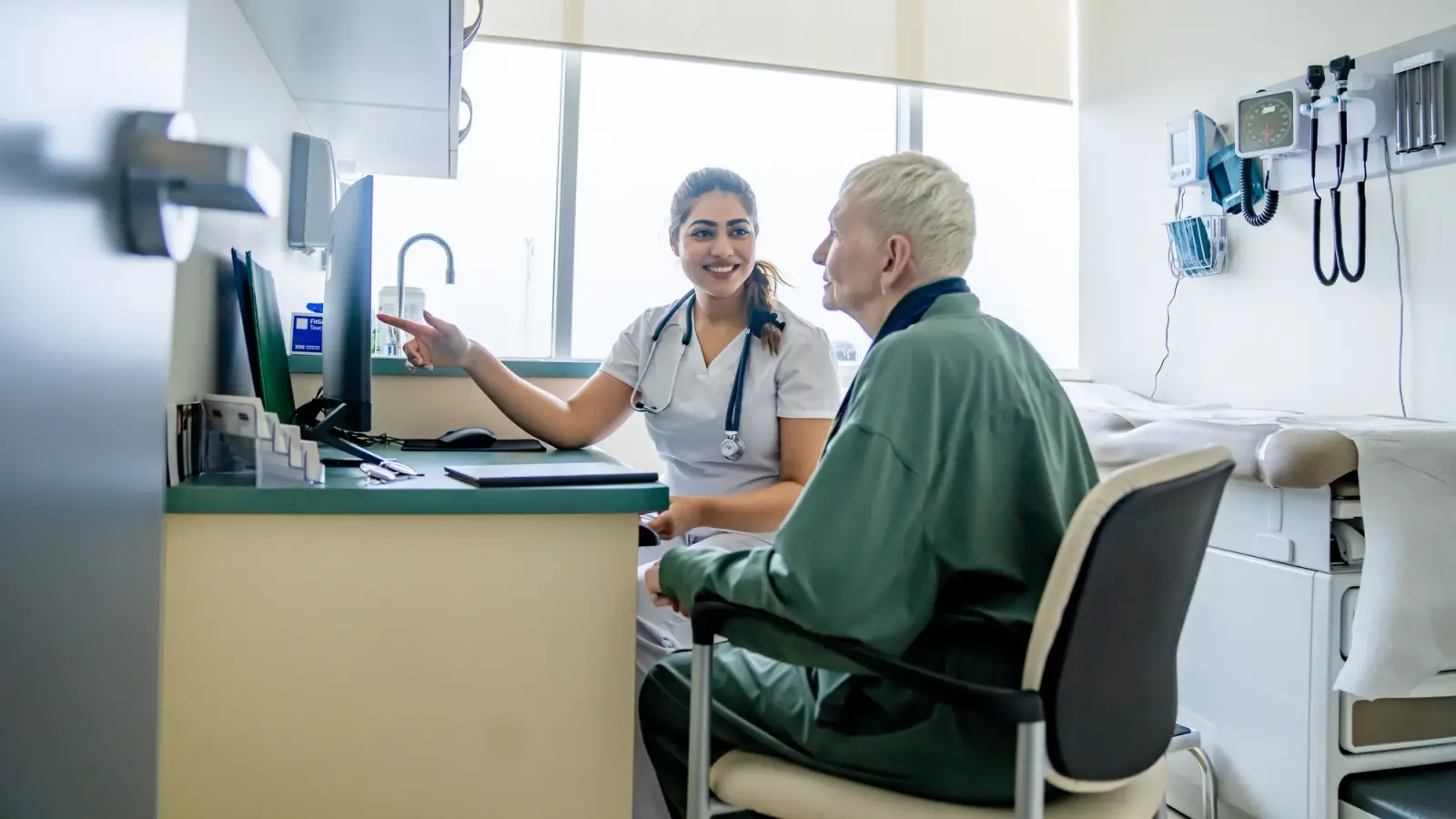 A woman talks with her doctor while they look at a desktop computer.