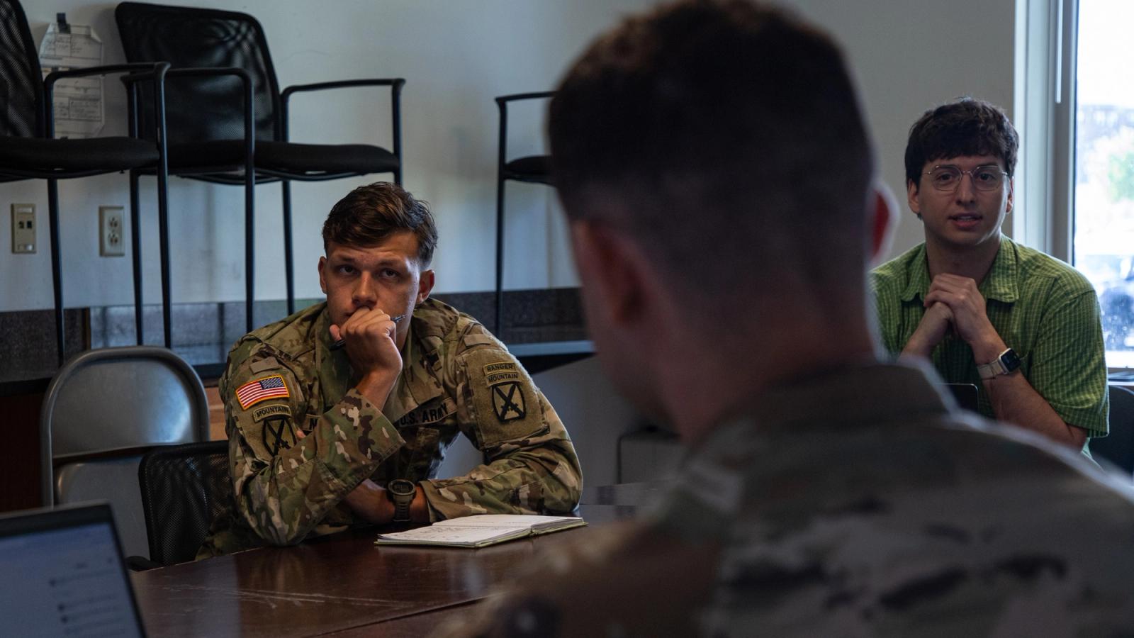 Two soldiers and a civilian discuss at a conference table.