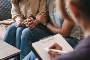  We see the hugging of a couple in therapy with the therapist from behind in the foreground.