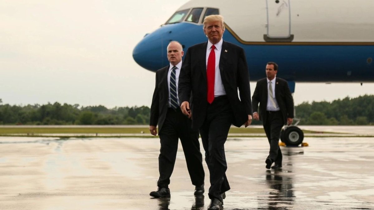 Three men, including a prominent figure, walking on wet tarmac near Air Force One.