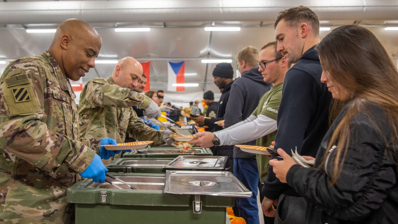 U.S. Army Command Sgt. Maj. Michael L. McLaughlin and Col. Richard J. Ikena Jr., serve a Thanksgiving meal to Soldiers on deployment at Camp Ādaži, Latvia.