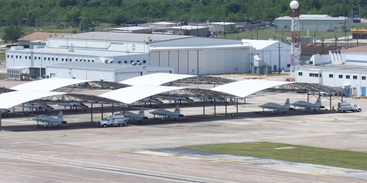 Planes sitting under open hangars in an airfield.